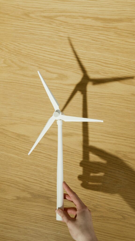 Close-up of a hand holding a small wind turbine model casting a shadow on a wooden surface.